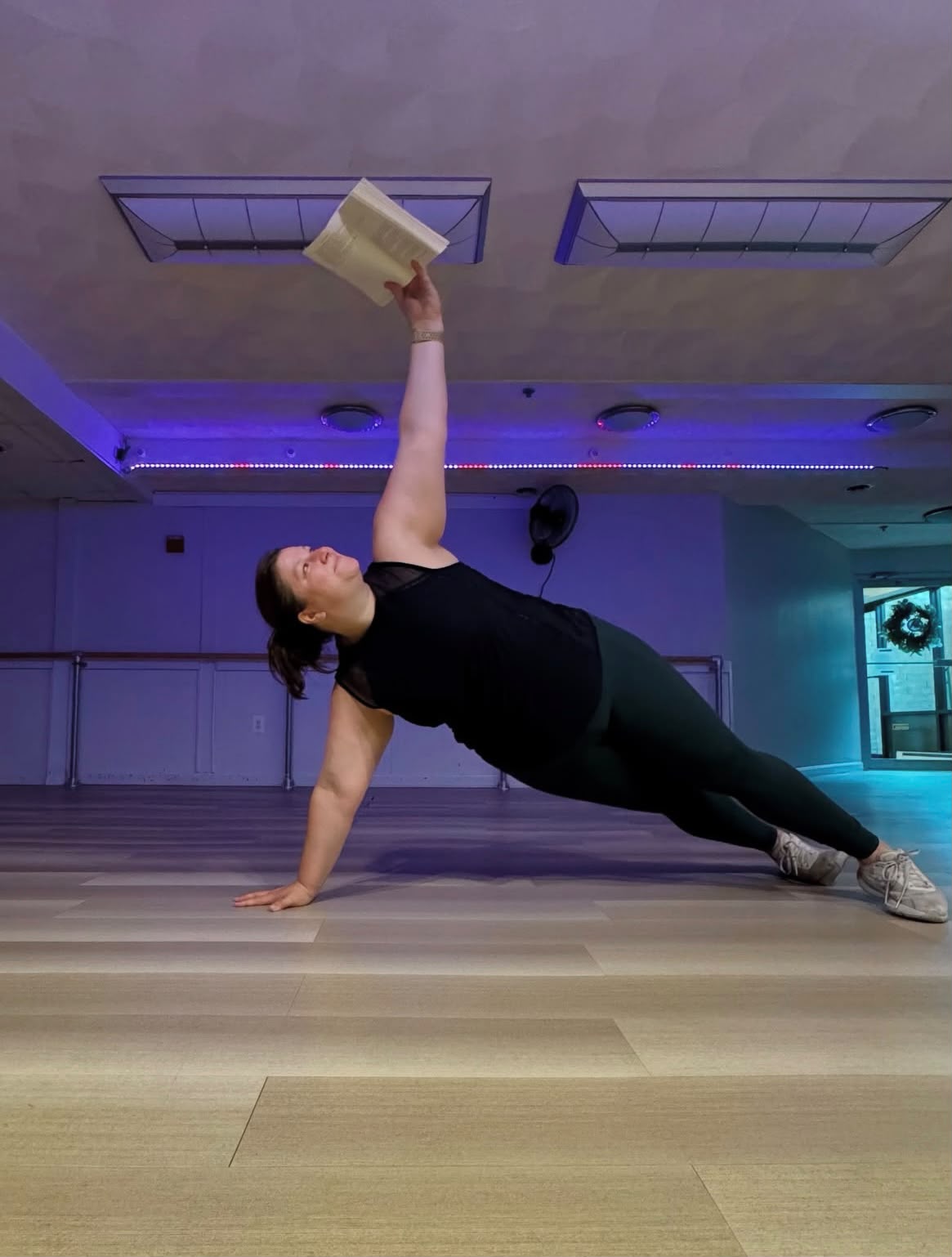 Diana holding a side plank while reading a book in the studio